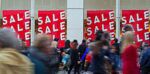 a busy high street with shoppers walking past a store with for sale signs on show