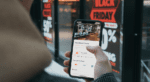 man stood outside a shop window whilst browsing on smartphone